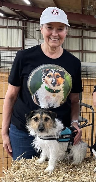 Photo of CJ and Moose at a barn hunt event, CJ wearing a custom dog t-shirt with Moose's portrait on a green background